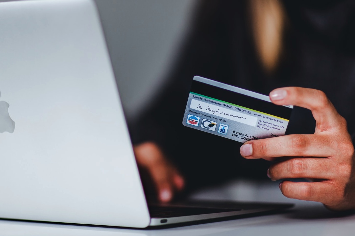 Personne tenant une carte bancaire à la main et s'apprêtant à payer sur son MacBook