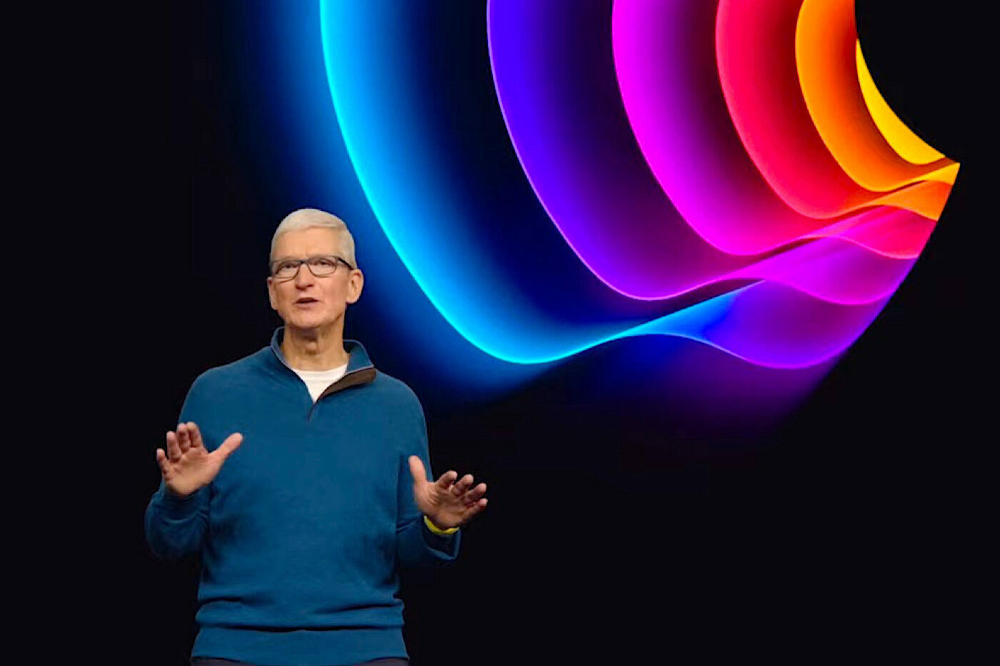 Tim Cook sur scène devant un fond avec pomme colorée