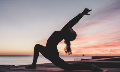 Femme en position de yoga face à la mer avec un soleil couchant