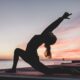 Femme en position de yoga face à la mer avec un soleil couchant