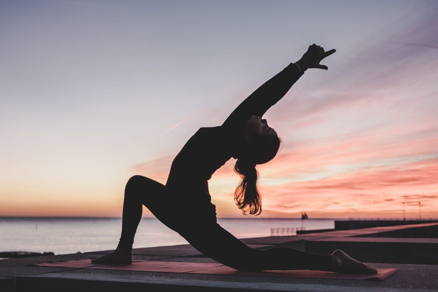 Femme en position de yoga face à la mer avec un soleil couchant